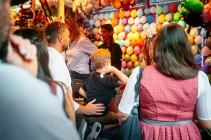 Ein Junge der auf dem Rosenheimer Herbstfest, an einem Ballonstand, knieend einen Pfeil wirft