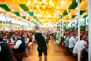 Speisen die auf einem Tablett von einem Mann durch die gefüllte Auerbräu-Festhalle, auf dem Rosenheimer Herbstfest, getragen werden