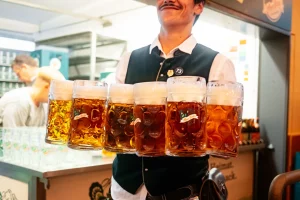 Männliche Bedienung auf dem Rosenheimer Herbstfest, die sechs gefüllte Auerbräu Bierkrüge trägt