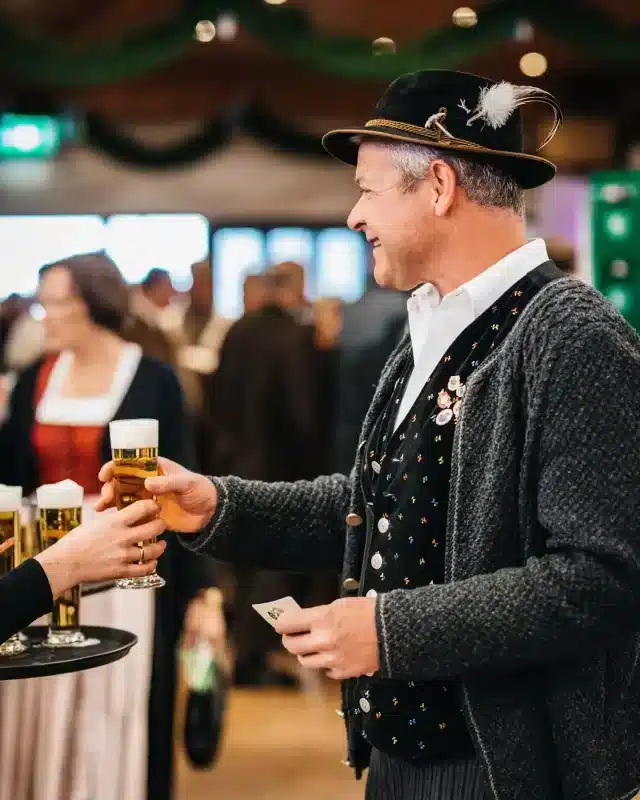 Hans Stocker in Tracht greift auf dem Rosenheimer Herbstfest nach einem, mit Auerbräu gefülltem, Bierglas